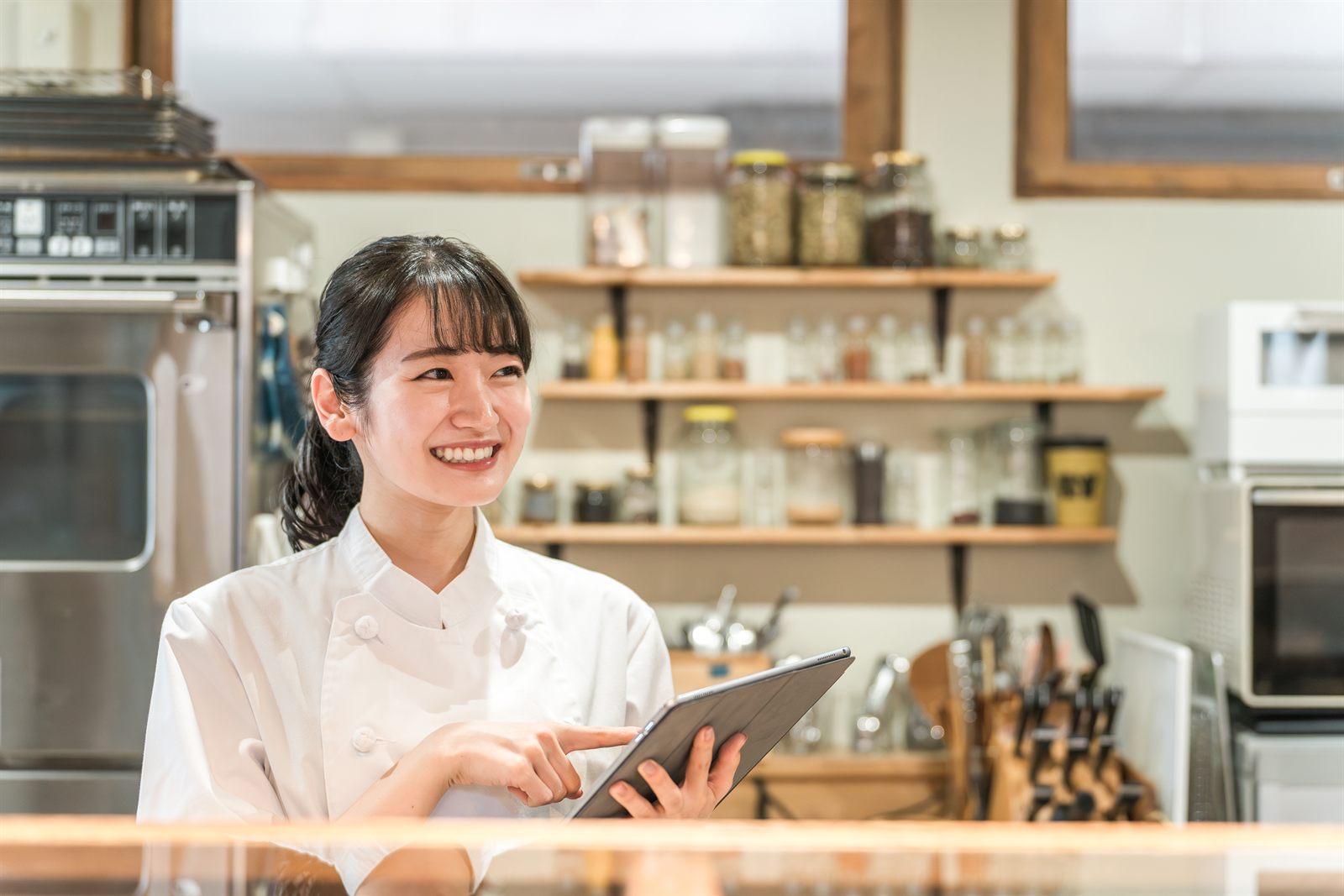 店内でタブレットを見ながら笑顔で立つ店主